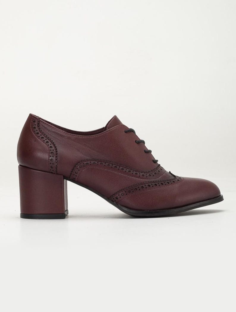 May include: Burgundy leather oxford-style shoe with a block heel. The shoe features decorative perforations along the seams and a lace-up closure. The heel measures approximately 2.5 inches.