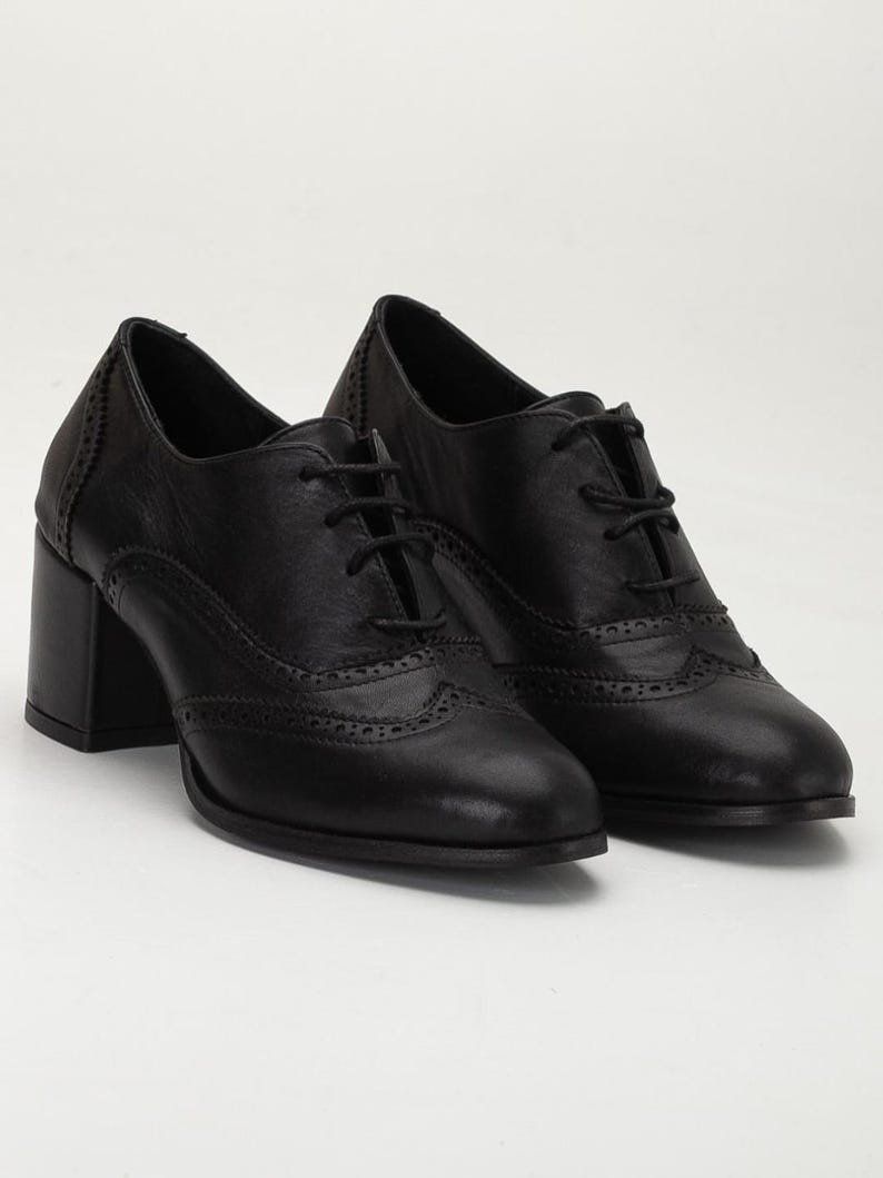 May include: A pair of black leather Oxford-style shoes with a block heel. The shoes feature decorative perforations along the toe and sides, and are laced up with black laces. The heels are approximately 3 inches high.