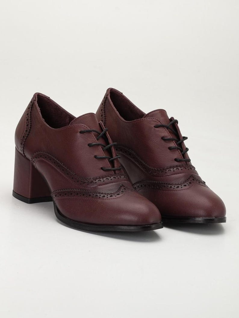 May include: A pair of burgundy leather Oxford-style shoes with a block heel. The shoes feature decorative perforations along the seams and a lace-up closure. The heels are approximately 3 inches high.