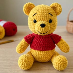May include: A handmade crochet stuffed bear toy featuring a bright yellow body and a vibrant red shirt. The bear has round ears, a small black nose, and embroidered black eyes and a smile. The texture is consistent with yarn stitches throughout.
