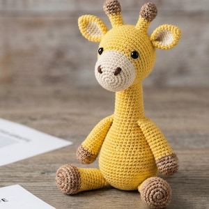 May include: A handmade crochet giraffe toy in yellow, beige, and brown. The giraffe has a long neck, small horns, and is sitting on a wooden surface. The toy is made with a tight stitch pattern, giving it a textured appearance.