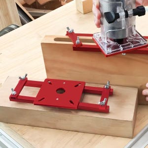 Könnte beinhalten: Ein rotes Fräsbasissystem mit verstellbaren Klemmen und einer transparenten Kunststoffbasis. Das System ist für die Holzbearbeitung konzipiert und wird in der Anwendung mit einem Elektrofäser gezeigt.