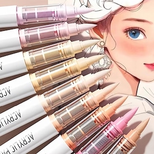 May include: A collection of acrylic paint pens in various pastel shades, including pinks, creams, and tans. The pens have white barrels with the words "ACRYLIC PA" visible. The image also features a stylized illustration of a woman with blue eyes.