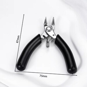 May include: A pair of silver metal pliers with black rubber handles. The pliers are 3 inches long and 3.4 inches high. The tool has a spring and is designed for cutting or gripping small objects.