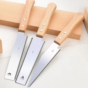 May include: Three hand saws with wooden handles and silver blades. The blades have a serrated edge and a small hole near the handle. The handles are attached with two silver rivets.