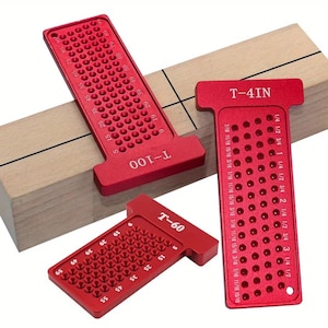 May include: Three red T-square tools with measurement markings and hole patterns. The tools are labelled T-100, T-60, and T-4IN. The tools are designed for woodworking and are placed on a light-coloured wooden block.