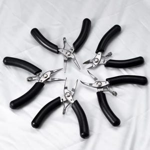 May include: A collection of six metal pliers with black, curved handles. The pliers are arranged in a circular pattern against a white background. The tools have a silver finish and are designed for precision work.