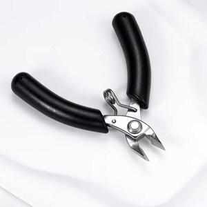 May include: A pair of black-handled wire cutters with a silver metal cutting head. The handles are curved and ergonomic. The tool is designed for precision cutting of wires and small objects.