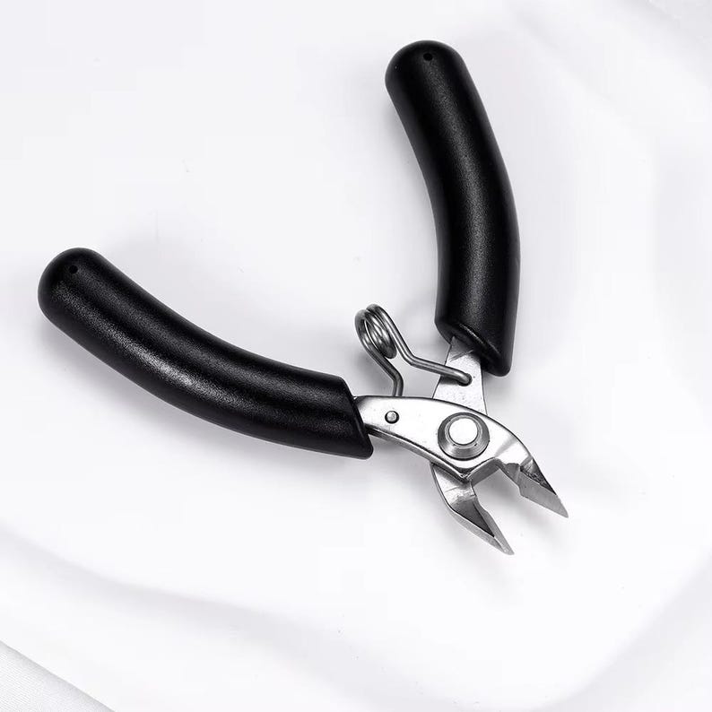 May include: A pair of black-handled wire cutters with a silver metal cutting head. The handles are curved and ergonomic. The tool is designed for precision cutting of wires and small objects.