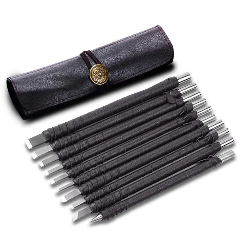 May include: A set of wood carving tools with black wrapped handles and silver blades, displayed with a black leather roll-up case. The case is secured with a brown cord and a decorative gold-colored button.