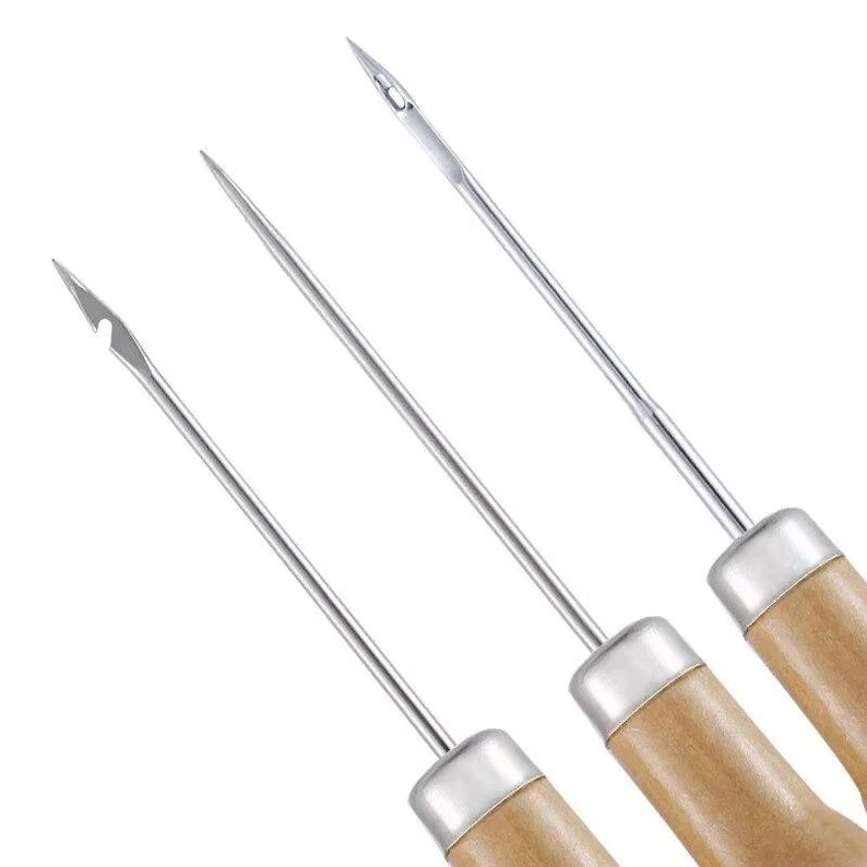 May include: Three steel needles with wooden handles. The needles have different tip designs, including a sharp point, a curved tip, and a needle with a small hook. The handles are light brown and cylindrical, with a silver metal band where the needle meets the handle.