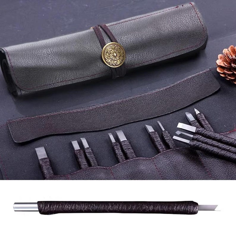 May include: A dark brown leather tool roll with a decorative brass button closure. The roll contains several metal carving tools with dark brown wrapped handles. The tools are arranged in a row, with the blades visible.