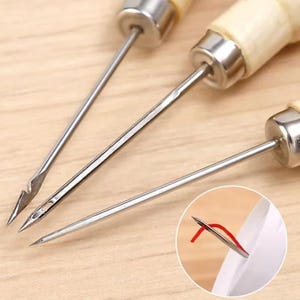 May include: Close-up of three sewing needles with wooden handles and metal tips. One needle has a curved tip, another has a small eye for threading, and the third is a simple pointed needle. A small inset shows a needle threaded with red thread.