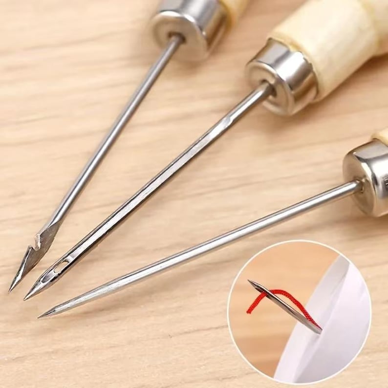 May include: Close-up of three sewing needles with wooden handles and metal tips. One needle has a curved tip, another has a small eye for threading, and the third is a simple pointed needle. A small inset shows a needle threaded with red thread.