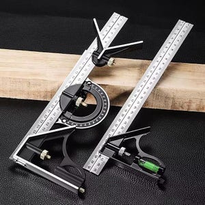 May include: A set of black and silver combination squares and protractor with measurement markings. The tools are placed on a wooden plank and a black surface. The protractor has a circular scale.