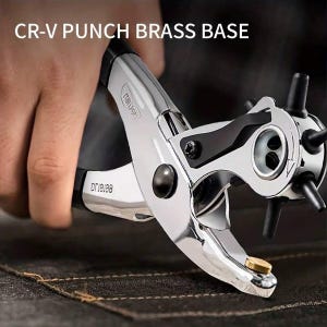 May include: A chrome CR-V punch brass base tool with black accents is held over a dark surface. The tool has a rotating head with multiple punch sizes and a brass base. The text "CR-V PUNCH BRASS BASE" is visible.