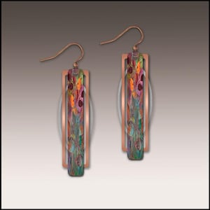 May include: A pair of copper-colored earrings with a rectangular design. The earrings feature a colorful, abstract pattern in shades of green, orange, and purple. The earrings have a hook closure.