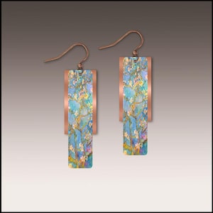 May include: A pair of rectangular earrings with a copper-colored frame. The center of each earring features a blue background with a floral design in white, yellow, and green. The earrings have a hook closure.