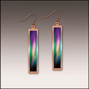 May include: A pair of copper-colored earrings with a rectangular design. Each earring features a vertical, colorful abstract design with shades of purple, green, and pink. The earrings have a hook closure.