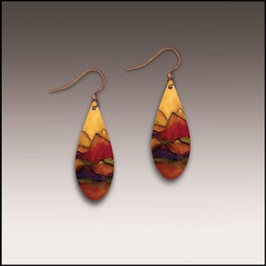 May include: A pair of teardrop-shaped earrings with a landscape design. The earrings feature a copper-colored hook and a painted scene of mountains in shades of yellow, red, and purple. The earrings are designed to dangle.