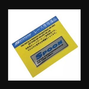 Puede incluir: Una pegatina rectangular amarilla con una cabecera azul que incluye el texto Spoon y caracteres japoneses. El cuerpo contiene el texto THIS PART(S) IS PRODUCED FOR RACETRACK USE ONLY. ANY OTHER USE VIOLATES THE LAW. Un emblema plateado dice SPOON TAKE PERFORMANCE TO THE LIMIT.