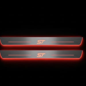 Może przedstawiać: Dwie podświetlane nakładki na progi drzwi z pomarańczowymi literami "ST". Płytki są srebrne z czerwoną poświatą na krawędziach, na czarnym tle. Akcesoria samochodowe.