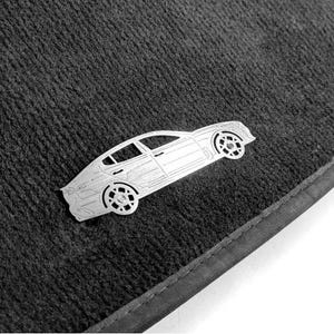 以下が含まれることがあります： シルバーの車のエンブレムが付いた濃い灰色の車のフロアマット。 エンブレムはセダンの詳細なアウトラインです。 マットはテクスチャード加工された表面とステッチされたボーダーを備えています。