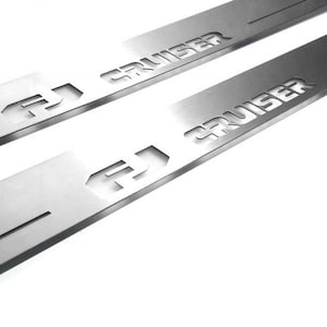 May include: Two silver metal FJ Cruiser door sill protectors. Each has the FJ logo and the word "CRUISER" cut out. The pieces are rectangular with a beveled edge and a slot cut into the side.