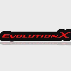 May include: A black sticker with the text "EVOLUTION X" in red. The sticker has a rectangular shape with rounded edges. The text is in a bold, sans-serif font. A shadow is visible.