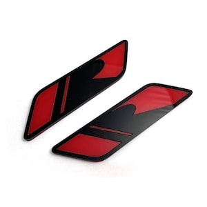 Puede incluir: Dos calcomanías rectangulares negras y rojas. Cada calcomanía tiene un fondo negro con un acento rojo. Las calcomanías están en ángulo y parecen estar hechas de un material brillante. El fondo es blanco.