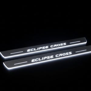 May include: Two illuminated, silver car door sills. The text "ECLIPSE CROSS" is displayed in white, centered on each sill. A white horizontal line is above the text. The sills are set against a black background.