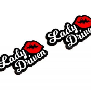 May include: Two black and white Lady Driven decals with a red lip graphic. The decals have a cursive font and a glossy finish. The image is on a white background.