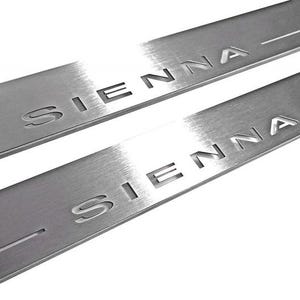 May include: Two brushed metal Sienna door sill protectors. The word "SIENNA" is cut out of the metal. The metal has a brushed finish and a horizontal groove.