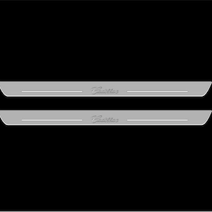 May include: Two silver car door sill plates with the Cadillac logo in a cursive font. The plates are rectangular with rounded edges and a thin, horizontal line. The background is black.