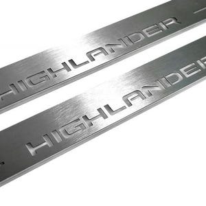 May include: Two brushed metal door sill protectors with the word "HIGHLANDER" etched into the surface. The protectors are rectangular and have a brushed metal finish. The text is in a sans-serif font.