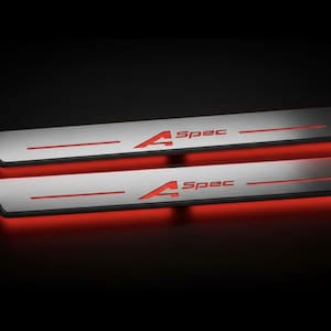 May include: Two illuminated car door sill plates. The plates are silver with red accents and the text "A Spec". The bottom of the plates have a red glow. The background is black.