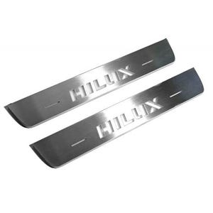 May include: Two stainless steel door sill protectors with the word "HILUX" cut out. The protectors are rectangular with curved edges and a brushed metal finish. They are designed for a vehicle.