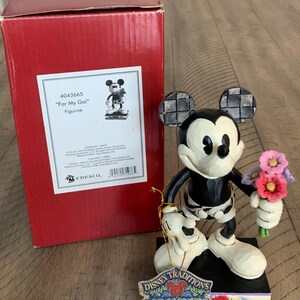 Op de afbeelding: Een Mickey Mouse-figuurtje dat een boeket roze, paarse en rode bloemen vasthoudt, staand op een zwarte voet met een Disney Traditions-label. Daarnaast staat een rode kartonnen doos met het label 4043665 For My Gal Figurine met een afbeelding.