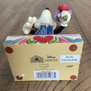 Op de afbeelding: Een Disney Traditions beeldje met een wit personage dat een boeket rode en paarse bloemen vasthoudt. De basis is cr&egrave;mekleurig met een rood hart, blauwe en groene accenten en tekst waaronder "For My Gal", "#4043665" en "Not A Toy".