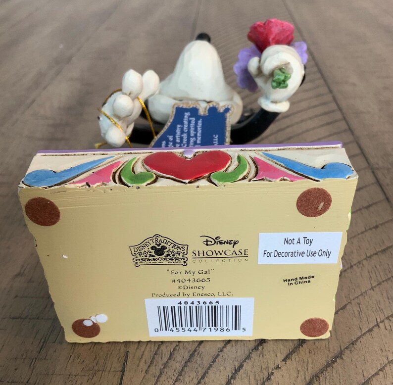 Op de afbeelding: Een Disney Traditions beeldje met een wit personage dat een boeket rode en paarse bloemen vasthoudt. De basis is cr&egrave;mekleurig met een rood hart, blauwe en groene accenten en tekst waaronder "For My Gal", "#4043665" en "Not A Toy".
