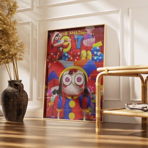 May include: A framed art print featuring a cartoon character with large eyes, wearing a colorful jester-like outfit. The artwork has a red background with the words "THE AMAZING" at the top. The print is displayed near a decorative vase and a woven side table.