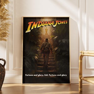 May include: Framed poster featuring the title "Indiana Jones" in yellow and red lettering. The artwork depicts a figure walking up stone steps towards a golden statue, surrounded by lush green foliage. The text "Fortune and glory, kid. Fortune and glory" is at the bottom.