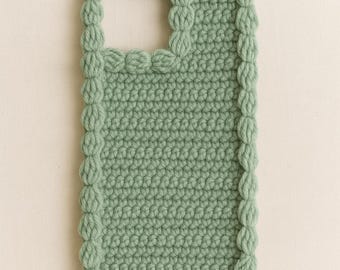 Puede incluir: Una funda de teléfono de ganchillo verde salvia. La funda presenta un patrón de puntada texturizada y un borde decorativo de puntos de burbuja. La abertura para la cámara es visible en la parte superior. La funda está diseñada para proteger un teléfono.