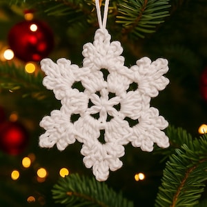 Puede incluir: Adorno navideño de copo de nieve blanco tejido a ganchillo, colgado de un hilo blanco. El copo de nieve está enfocado, con un diseño detallado y calado. Bolas de Navidad rojas y agujas de pino verdes en el fondo borroso.