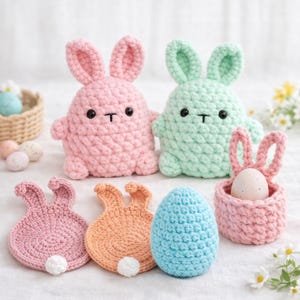 May include: A collection of handmade crochet Easter decorations. The image features two plush bunny figures, a pink and a mint green one, along with bunny-shaped coasters, an egg-shaped decoration, and a basket holding an egg.