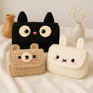 May include: Three handmade crochet purses in the shape of animals. A black cat purse with large white eyes, a tan bear purse, and a white bunny purse. Each purse has a flap closure and is made of textured yarn.