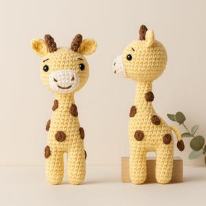 Könnte beinhalten: Zwei handgefertigte gehäkelte Giraffen-Spielzeuge. Die Giraffen sind gelb mit braunen Flecken und Akzenten. Sie haben kleine, braune Hörner und eine weiße Schnauze. Eine Giraffe blickt nach vorne, die andere im Profil. Die Spielzeuge stehen vor hellem Hintergrund.