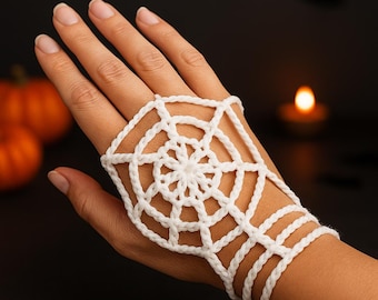 May include: A white crochet spiderweb hand accessory. The intricate design features a central circular web with radiating lines and connecting wrist straps. The accessory is designed to be worn on the hand, with the web design covering the back of the hand.