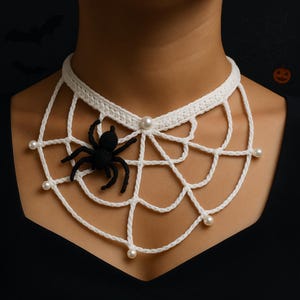 Może przedstawiać: Biały szydełkowy naszyjnik z motywem pajęczyny. Naszyjnik posiada czarnego pająka i akcenty z imitacji pereł. Ten dodatek o tematyce Halloween to wyjątkowy element.