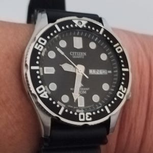 May include: A Citizen Quartz watch with a black dial, luminous markers, and a date display. The watch has a black rotating bezel and a black rubber strap. The watch is water resistant to 200m.